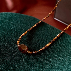 Macro shot of faux tiger eye beaded necklace with large red-brown gemstone on green velvet