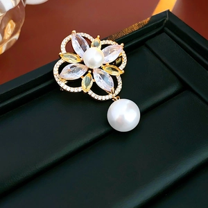 Macro shot of gold-plated flower brooch with zircons and drop-shaped pearl detail