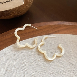 Detailed view of cream pearlescent C-shaped earrings with floral wavy edges on linen