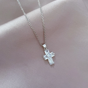 Macro detail of a silver cross pendant with clear cubic zirconia on satin fabric