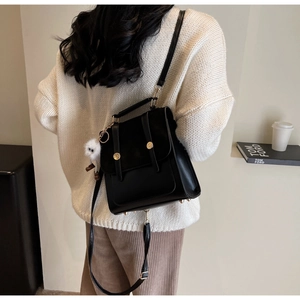 Lifestyle shot of black leather backpack featuring gold hardware and a white plush charm
