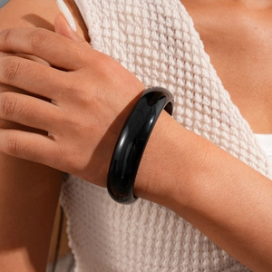 Close-up of a polished black resin bangle with mirror finish on a model's wrist