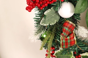 Close-up of artificial Christmas wreath with red berries and plaid ribbon detail