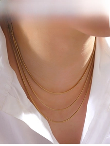 Detailed view of layered gold snake chain necklaces worn over a white collared shirt