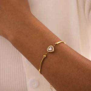 Close-up of heart-shaped 18K gold bracelet with clear zircon stones on woman's wrist