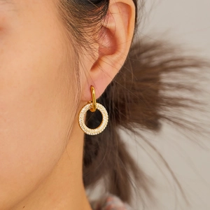 Macro detail of gold-plated U-shaped hoop earrings featuring a pavé-set zircon circle charm