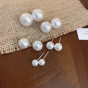 Macro view of minimalist white pearl stud earrings set in five varying sizes on rustic wood