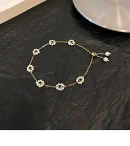 Detail of French vintage gold bracelet with emerald green stones and white flower petals