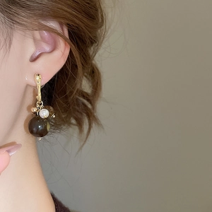 Detail of elegant gold hook earring with brown bead and white pearl on model