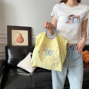 Détail d'un sac à main en oxford jaune brodé avec anses tissées et motifs papillon