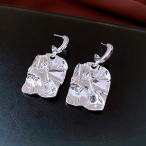 Detailed view of silver ginkgo-inspired earrings with crumpled texture on black leather
