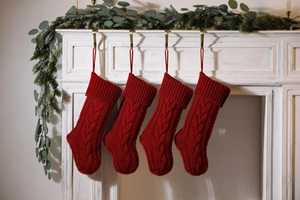 Set of four red cable knit Christmas stockings hanging on a decorated fireplace mantel