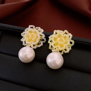 Detailed macro view of yellow woven flower earring with large white pearl on dark silk