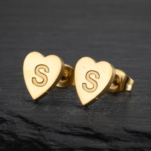 Minimalist gold heart-shaped stud earrings featuring engraved uppercase letter S detail