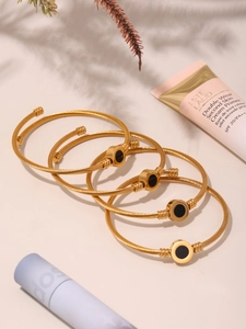 Detail of five-piece gold twisted rope bracelets with black round accents on beige background