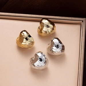 Detailed view of textured gold and silver organic shape earrings on a beige velvet tray