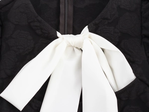 Detailansicht des schwarzen Kleides mit Rosen-Jacquard, weißer Schleife und Reißverschluss