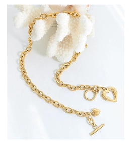 Detail of gold chunky chain necklace with heart charms and OT toggle clasp on coral
