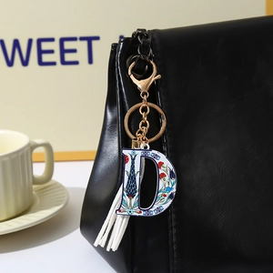 Detail of letter D keychain with floral patterns and white tassel on a black leather bag
