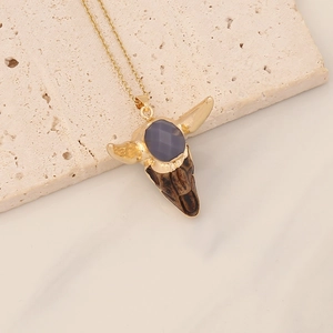 Detailed close-up of a vintage bull skull pendant with dark gemstone on gold necklace