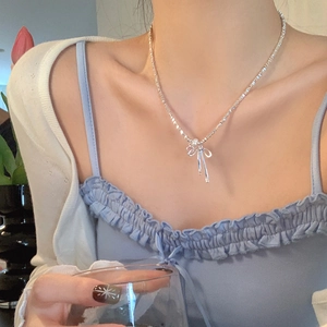 Close-up of a silver bow necklace with a pearl pendant on a model wearing a blue dress