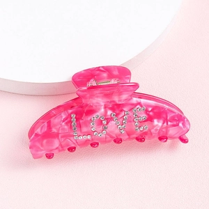Close-up of pink hair claw clip with rhinestones spelling LOVE on a soft background