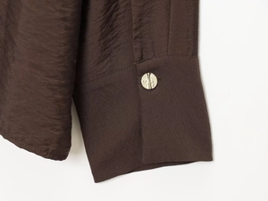 Detail of dark brown satin shirt cuff featuring a textured gold button and smooth fabric
