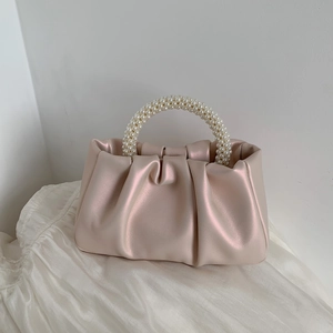 Close-up of pink cloud pleated handbag featuring elegant faux pearl handle on silk