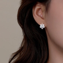Detailed close-up of a silver five-petal flower earring with zircons on a model's ear