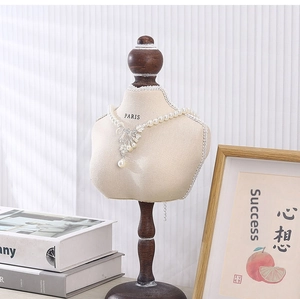 Detail of pearl necklace with floral tassel pendant on beige velvet bust display stand