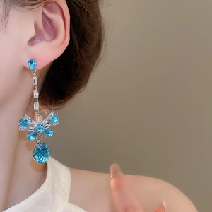 Detail of model wearing silver earrings with blue pear-shaped zircon and floral pendant