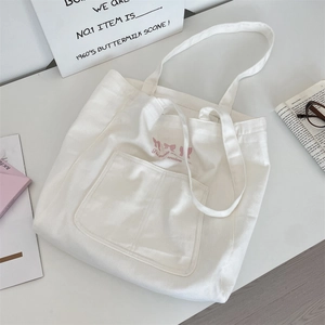 Detail shot of white canvas tote bag featuring pink bow embroidery and front square pocket