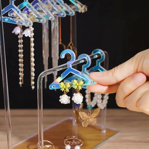 Iridescent acrylic earring stand with clothes hanger hooks showing hand placing jewelry
