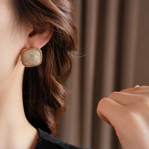 Close-up of square gold earrings with pavé crystals on model with brown background