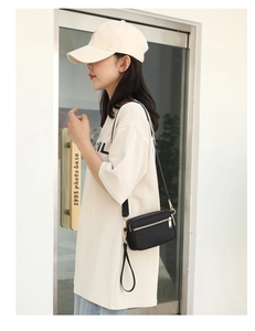 Model wearing a compact black multi-compartment crossbody bag with gold zippers