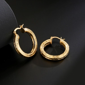 Textured gold-plated geometric round hoop earrings on a black reflective background