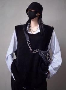 Detail of a black knitted vest paired with a striped shirt and silver chain necklace