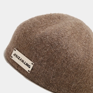 Close-up of wool beret with JISIZAN.LING silver metal logo and knit texture details