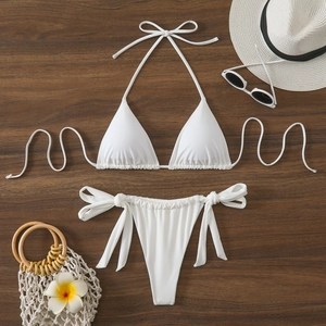 Flat lay di bikini a triangolo bianco con cappello e accessori da spiaggia su legno