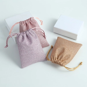 Detail of pink, purple, and gold glitter drawstring jewelry pouches on white display boxes