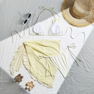 Three-piece yellow bikini set with mesh beach skirt and floral detail laid on white fabric