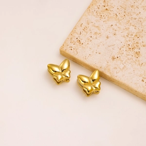 Detailed view of gold butterfly stud earrings on a textured decorative beige stone
