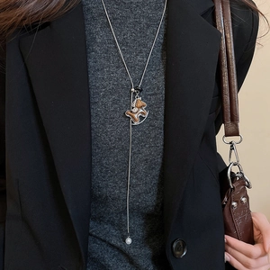 Close-up of a brown horse pendant necklace styled on a black suit and grey turtleneck