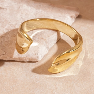 Detailed close-up of shiny gold textured cuff bracelet with organic wave patterns