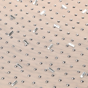 Close-up of beige mesh fabric with round and rectangular rhinestones on the slim dress