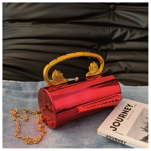 Detail of red cylinder evening bag featuring golden lion head handles and chain strap