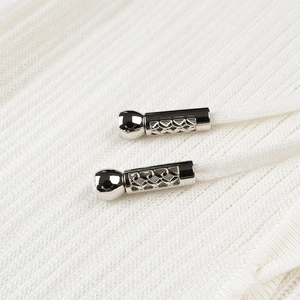 Detail of silver metallic drawstring toggle with geometric cutout on white knit fabric