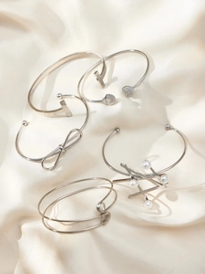 Macro shot of silver geometric bangles with pearls and bow charms on silk fabric