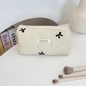 Close-up of beige quilted makeup bag with black bow embroidery and Suzakka label