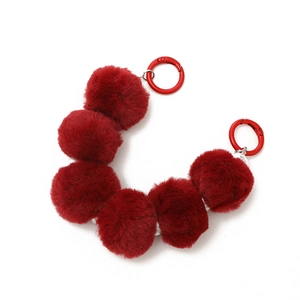 Red plush faux fur ball phone wrist strap with dual metal rings on white background